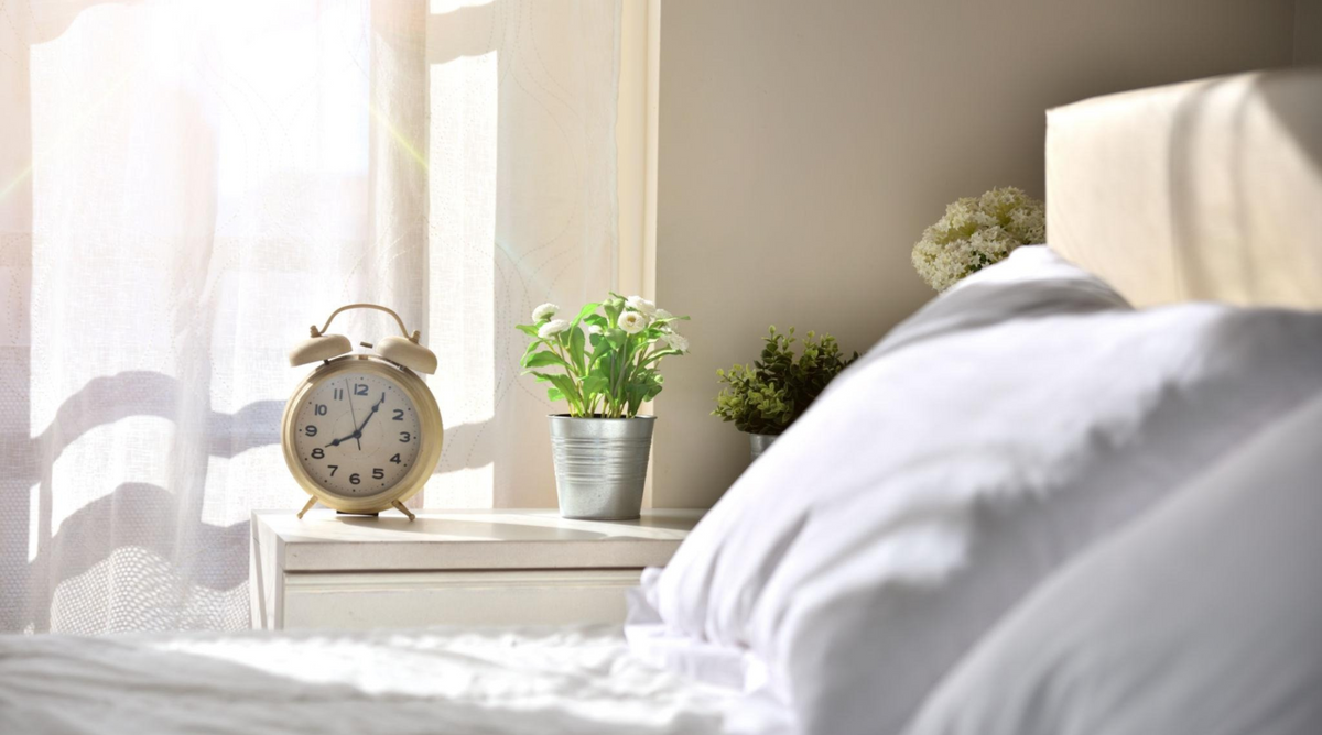 Cosy autumn bedroom with an alarm clock on the bedside table, soft bedding and warm morning light, illustrating the clocks going back.
