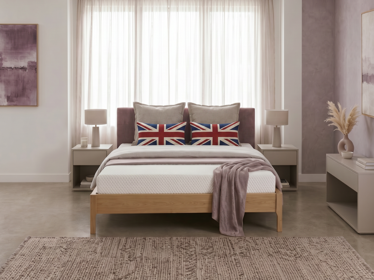 A bed with a white quilted mattress and matching white bedding, styled in a modern bedroom with a mauve wall, a Union Jack accent pillow, and light nightstands.